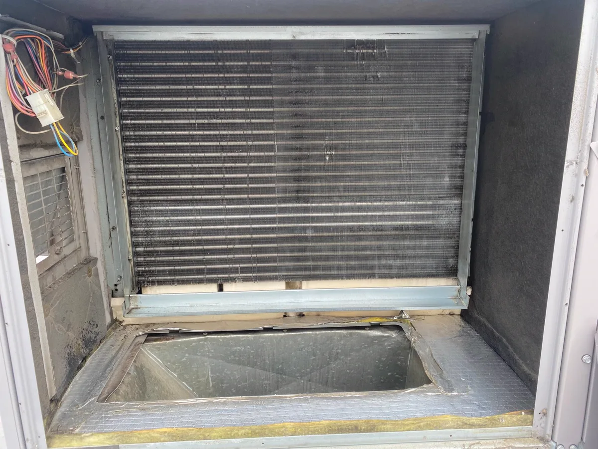 An access panel open on a packaged rooftop unit, showing the coil and the drain pan below it.