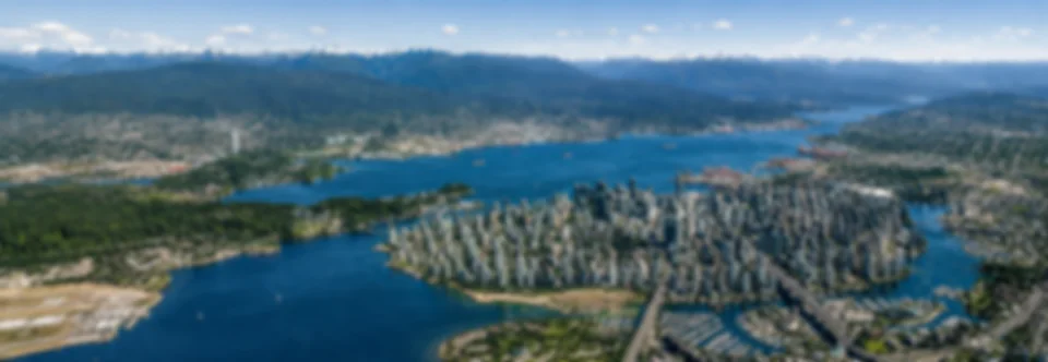 A lightly blurred stylized aerial panorama of Vancouver, its harbour, and surrounding mountains.